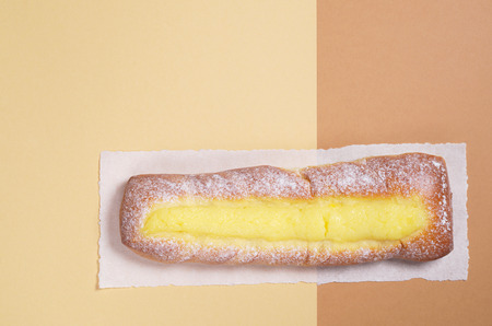 Sweet bun with custard sprinkled powdered sugar on paper located on two-tone  background, top view...