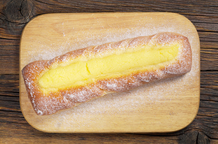 Homemade bun with custard, sprinkled icing sugar on cutting board located old wooden table, top view