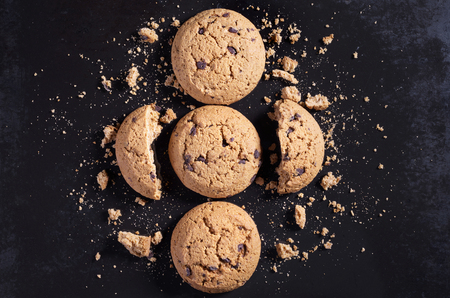 Oatmeal cookies with chocolate, whole, broken and crumbs on the background of old black metal, top viewの写真素材