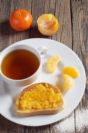 Cup of tea and toasted bread with tangerine jam in plate on rustic wooden table, high angle viewの写真素材