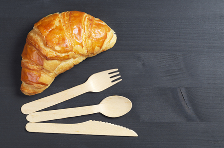 Croissant and wooden cutlery on black background, top view with copy spaceの写真素材