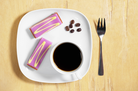 Cup of coffee and tasty cake, topped with decorated purple fondant icing in plate old wooden table, top viewの写真素材