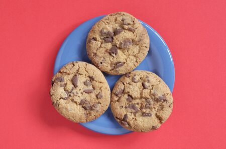 Chocolate chip cookies on a blue plate on a red background, top view