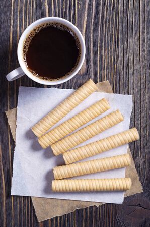 Chocolate waffle rolls and cup of coffee on brown wooden table, top viewの写真素材