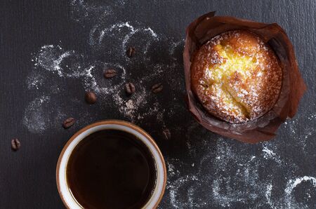 Coffee in a cup with a muffin on a black stone background, top viewの写真素材