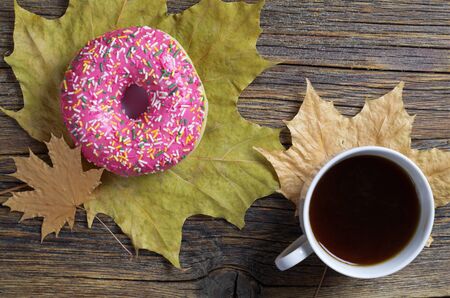 Pink donut, coffee cup and autumn leaves on old wooden background, top viewの写真素材