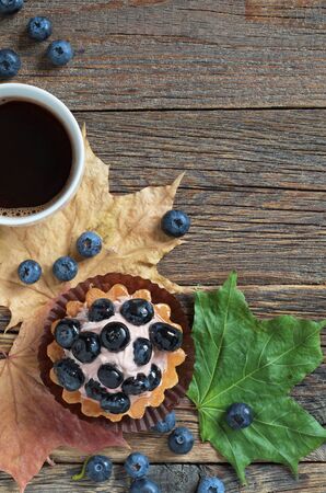 Blueberry cake with berries and coffee cup and autumn maple leaves on old wooden table. Top view with copy spaceの写真素材