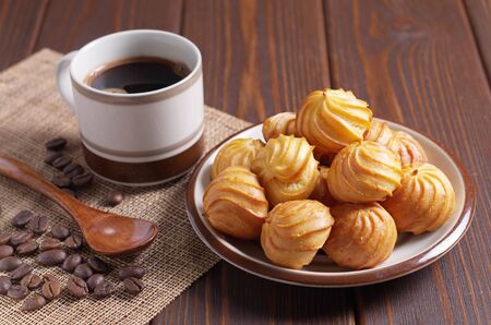Custard cakes in plate and cup of coffee on brown wooden table