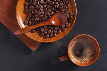Cup of hot coffee and beans in wooden saucer on black background, top viewの写真素材