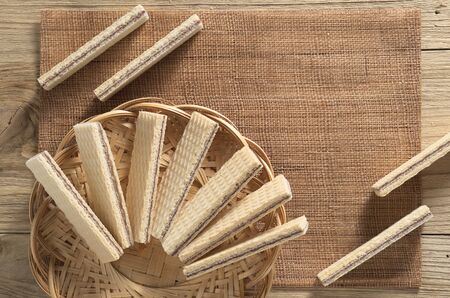 Wafers with chocolate in wicker plate an near located on the wooden table, top viewの写真素材