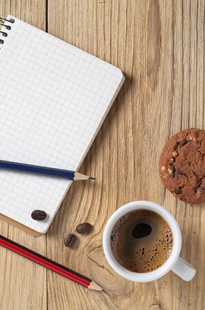 Notebook, pencils and coffee with cookies on wooden table, top viewの写真素材
