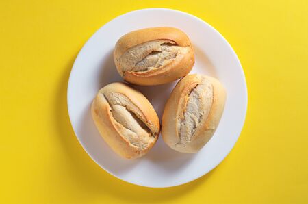 French buns on a white plate on yellow background, top view