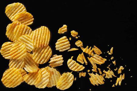 Crispy potato chips whole and broken on a black background, top viewの写真素材