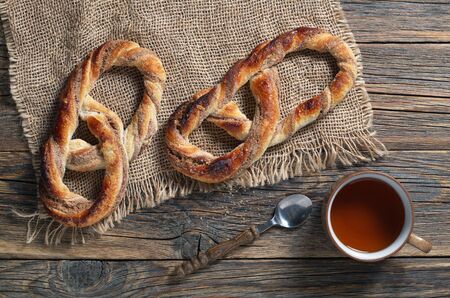 Sweet pretzels and cup of tea on rustic wooden table, top view