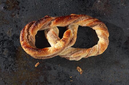 Single fresh pretzel with sugar on grunge iron background close-up, top view