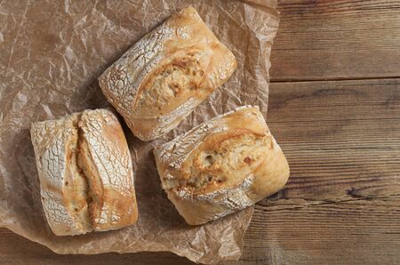 Loaves of small ciabatta bread on crumpled paper on wooden table, top view