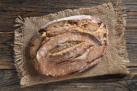 Loaf of rye bread on rustic wooden table with burlap, top view
