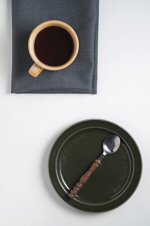 Cup of coffee and empty dark plate with spoon on white table, top view の写真素材