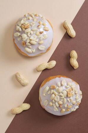 Glazed bun with peanuts on two-tone background, top view
