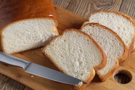 Sliced wheat bread and knife on a cutting board close-up