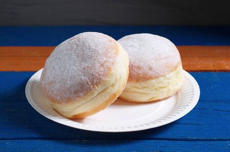 German donuts berliner with powdered sugar on a paper plate on colored wooden tabled close-up. Disposable eco paper tablewareの写真素材