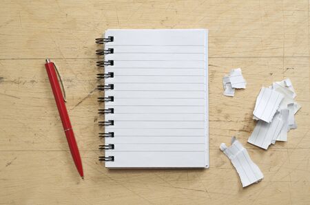 Opened notebook, red pen and torn paper on old wooden background, top view