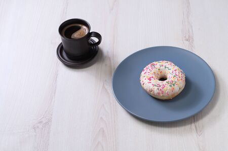 Cup of coffee and delicious donut with icing and sprinkles on grey plate on table. Copy spaceの写真素材