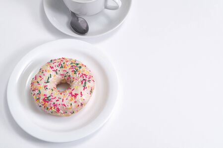 Donut with icing and sprinkles on a plate and cup on white table. High angle view. Copy spaceの写真素材
