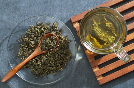 Cup of green tea with dried leaves on a cloth surface, top view