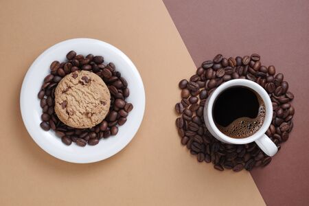 Chocolate chip cookie, cup of coffee and beans on two-tone brown background, top viewの写真素材