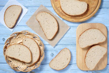 Slices of fresh bread on a plate end cutting board on wooden table as background, top view