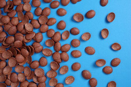 Chocolate cereals as background on blue. Glazed corn flakes in shape of shells. Top viewの写真素材