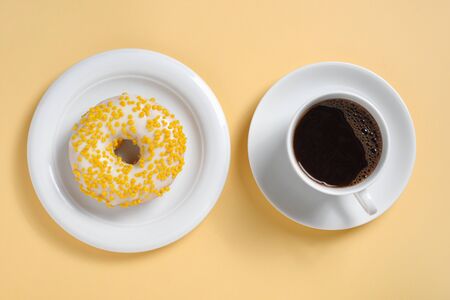 Donut with sprinkles on a plate and cup of coffee on yellow background, top viewの写真素材