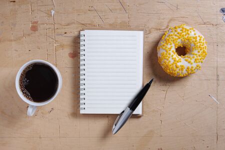 Notebook, cup of coffee and donut on wooden background, top view