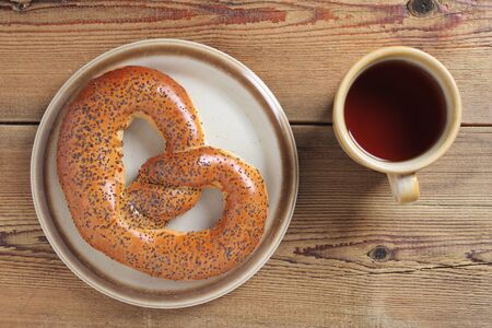 Poppy pretzel on a plate and cup of tea on wooden background, top view