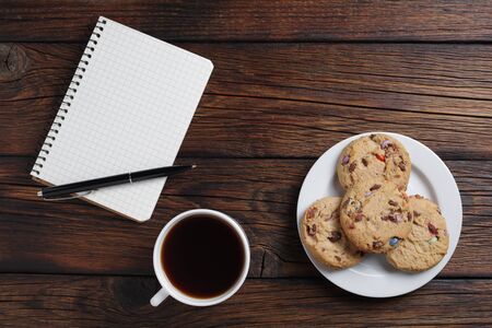 Cup of coffee, cookies and notebook with pen on wooden background, top view