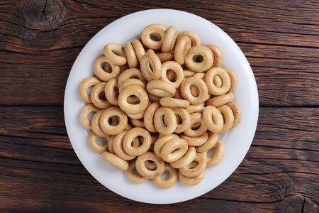 Small dry bagels on a plate on wooden background, top view