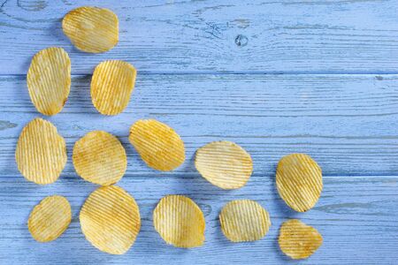 Ribbed potato chips on blue wooden table, top view