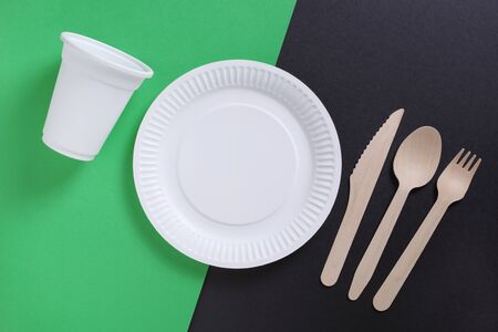 Paper plate, glass, wooden spoon, fork and knife on two-tone background, top viewの写真素材