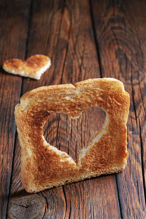 Toast with a heart-shaped cut on wooden background close-up