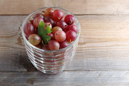 Ripe red gooseberries in glass on wooden background