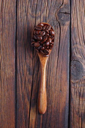 Roasted coffee beans in a wooden spoon on the table, top viewの写真素材