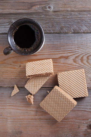Wafers with boiled condensed milk and cup of coffee on wooden background, top view