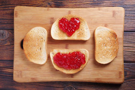 Toasted bread with strawberry jam on cutting board on wooden table, top view