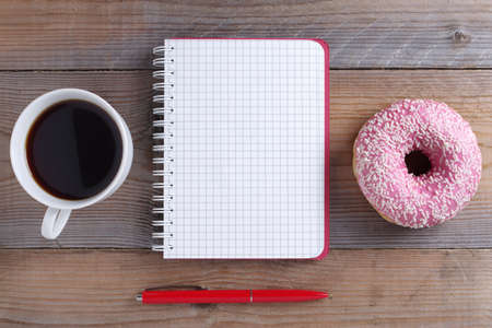 Directly above view of notebook and pink donut with cup of coffee on wooden backgroundの写真素材