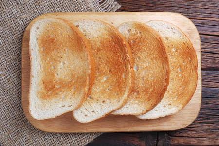 Roasted white bread on cutting board on the wooden table, top view