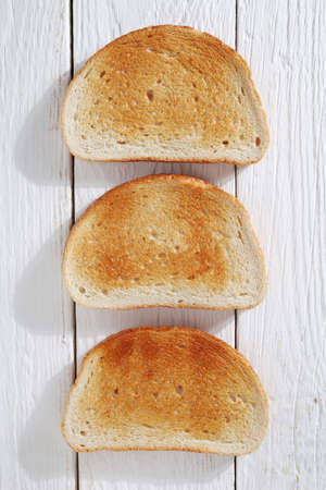 Slices of roasted bread on white wooden background, top view