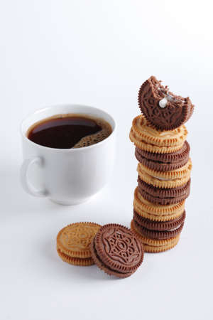 Stack of sandwich-biscuits filled with cream and cup of coffee on white background