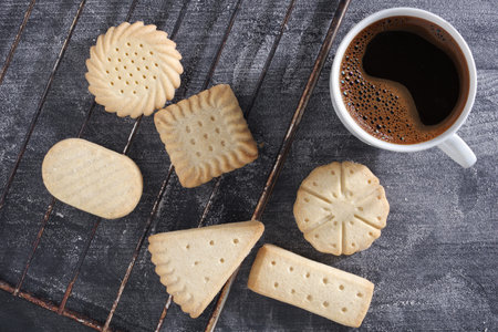 Various cookies and cup of coffee on black table with flour, top view