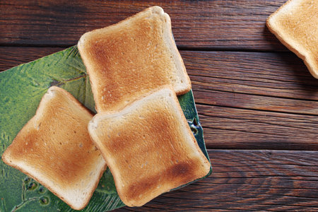 Slices of toasted bread on green ceramic board on wooden background, top viewの写真素材